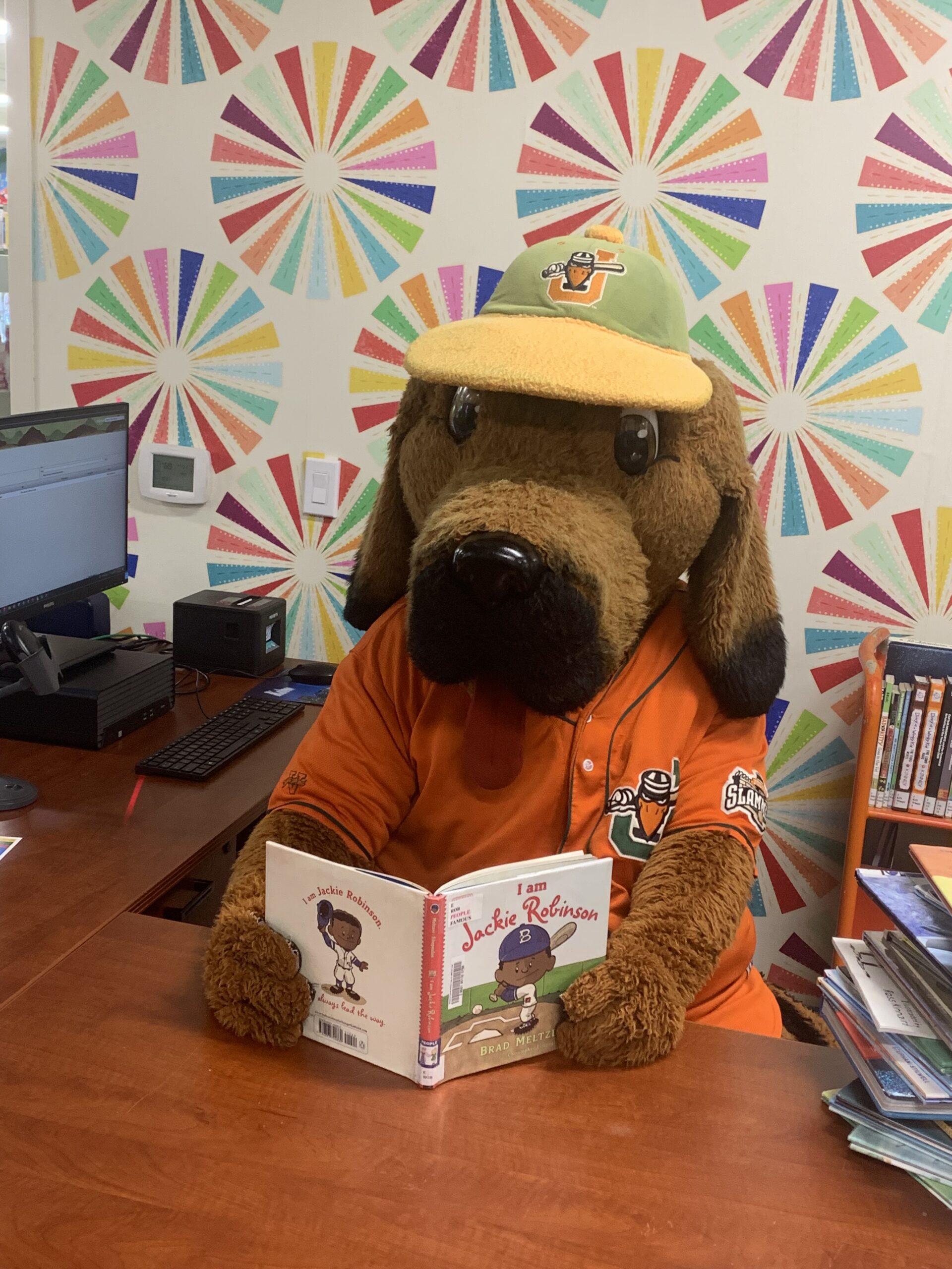 Image of Spikes the Joliet Slammers mascot catching up on some reading at the library